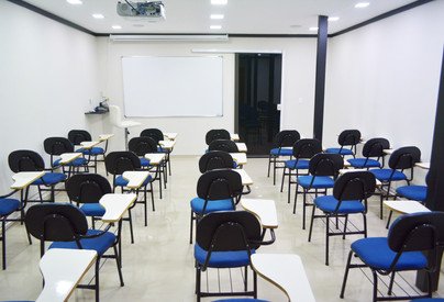 Auditório com cadeiras azuis com braço de apoio voltadas para o quadro