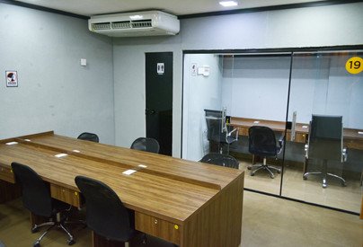 Sala privativa com bancada de madeira, cadeiras de escritório e divisórias de vidro